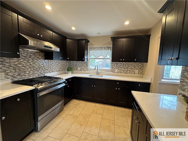 kitchen with tasteful backsplash, light countertops, stainless steel gas stove, a sink, and under cabinet range hood