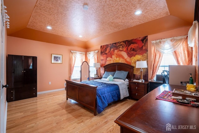 bedroom with multiple windows, light wood-type flooring, a raised ceiling, and baseboards