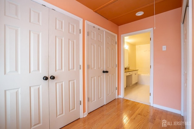 unfurnished bedroom with two closets, baseboards, light wood-style floors, and attic access