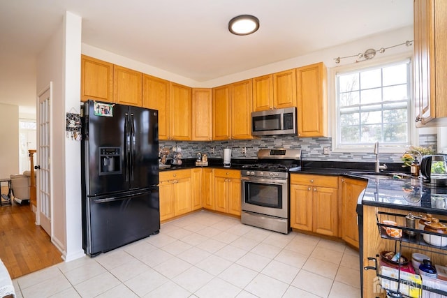 kitchen with tasteful backsplash, appliances with stainless steel finishes, dark countertops, and a sink