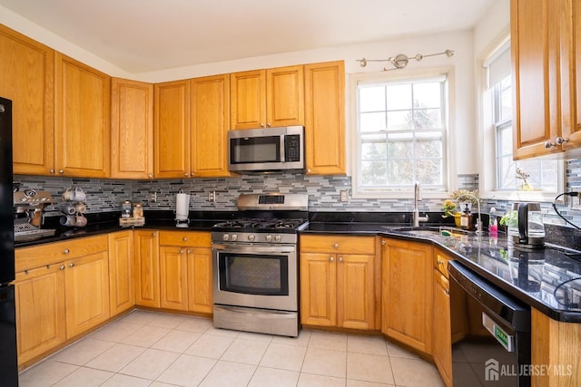 kitchen featuring light tile patterned floors, dark stone counters, a sink, appliances with stainless steel finishes, and tasteful backsplash