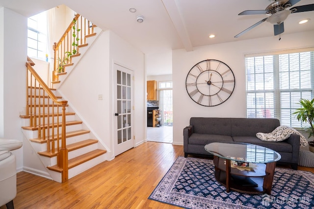 living area with stairway, plenty of natural light, light wood-style flooring, and a ceiling fan