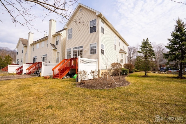 back of property with a yard, a wooden deck, and a chimney