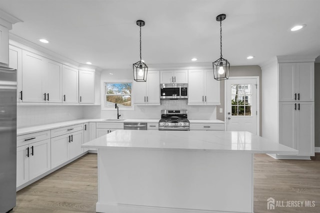 kitchen featuring decorative light fixtures, stainless steel appliances, light wood-style floors, white cabinets, and a kitchen island