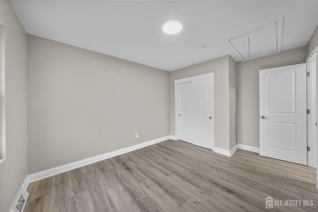 unfurnished bedroom featuring visible vents, light wood-style floors, baseboards, a closet, and attic access