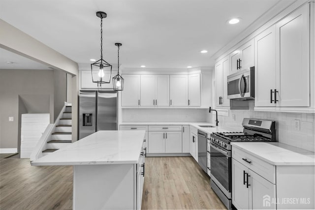 kitchen featuring light stone counters, stainless steel appliances, a kitchen island, white cabinetry, and decorative light fixtures