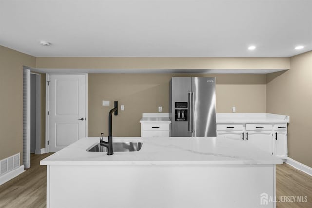 kitchen featuring high end refrigerator, a sink, visible vents, light countertops, and light wood finished floors