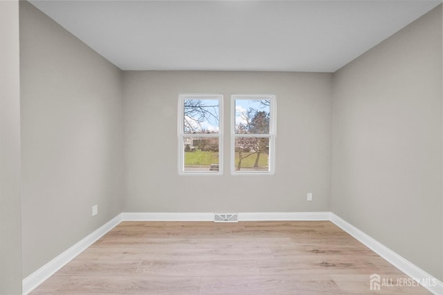 spare room with light wood-type flooring, visible vents, and baseboards