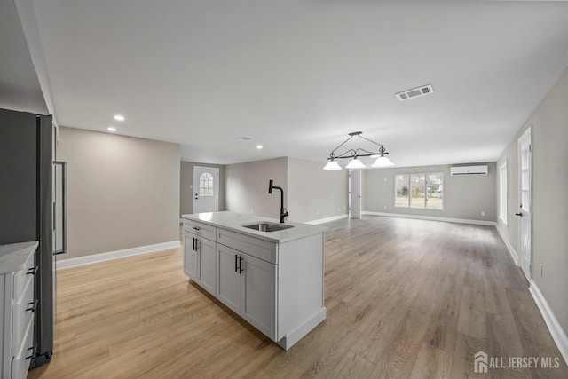 kitchen featuring light countertops, visible vents, open floor plan, a sink, and an island with sink