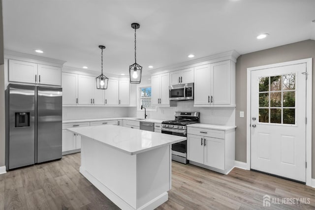 kitchen featuring light stone counters, a center island, stainless steel appliances, hanging light fixtures, and white cabinetry