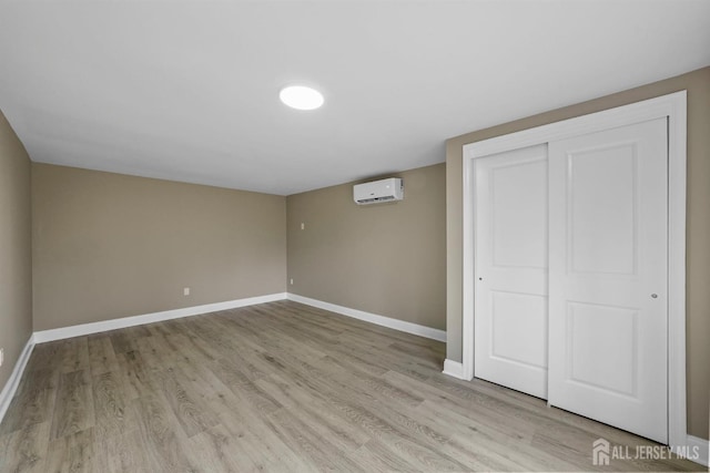 unfurnished bedroom with a closet, a wall mounted air conditioner, light wood-style flooring, and baseboards