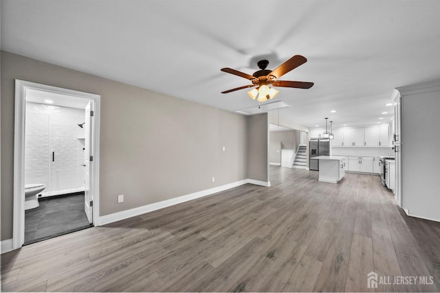 unfurnished living room with ceiling fan, wood finished floors, stairs, and baseboards