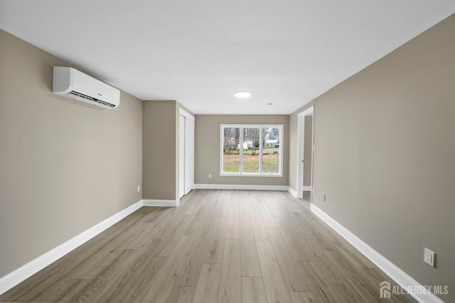 spare room featuring light wood-type flooring, baseboards, and an AC wall unit