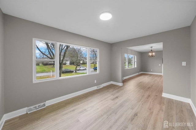 empty room with light wood-type flooring, visible vents, a notable chandelier, and baseboards