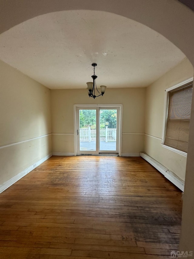 spare room featuring a chandelier, a baseboard heating unit, and dark hardwood / wood-style flooring