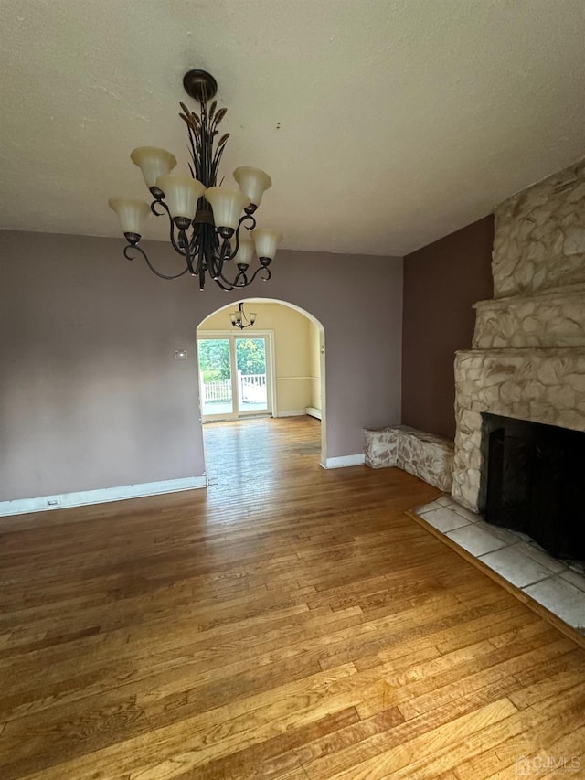 unfurnished dining area featuring an inviting chandelier, wood finished floors, a fireplace, baseboards, and arched walkways