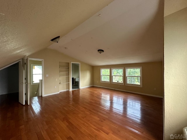 interior space featuring built in shelves, hardwood / wood-style flooring, a textured ceiling, and lofted ceiling