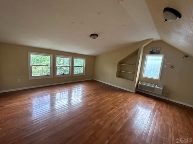 bonus room with wood finished floors, baseboards, a wall mounted AC, and lofted ceiling