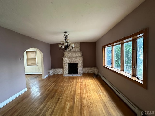 unfurnished living room featuring baseboard heating, baseboards, an inviting chandelier, wood finished floors, and arched walkways