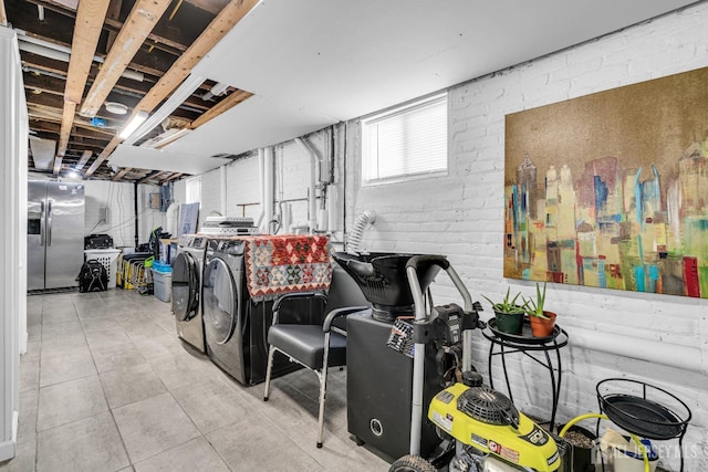 basement featuring brick wall, washing machine and dryer, stainless steel fridge, and light tile patterned floors