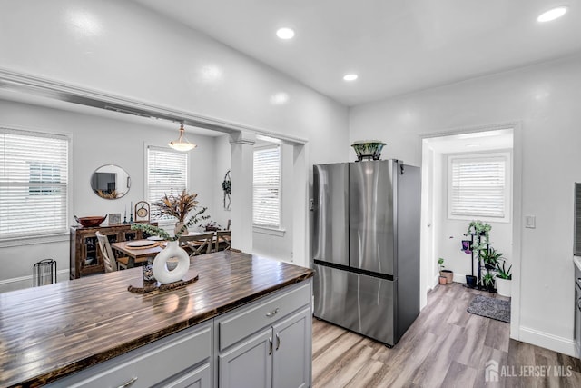 kitchen featuring light wood-type flooring, stainless steel refrigerator, hanging light fixtures, and wooden counters