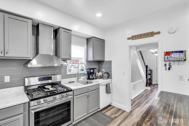 kitchen featuring gray cabinetry, stainless steel range with gas stovetop, sink, dishwasher, and wall chimney range hood