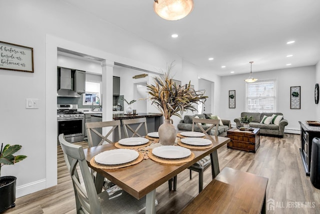 dining room with light wood-type flooring, ornate columns, sink, and baseboard heating