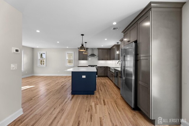 kitchen featuring a center island, light hardwood / wood-style flooring, hanging light fixtures, wall chimney range hood, and appliances with stainless steel finishes