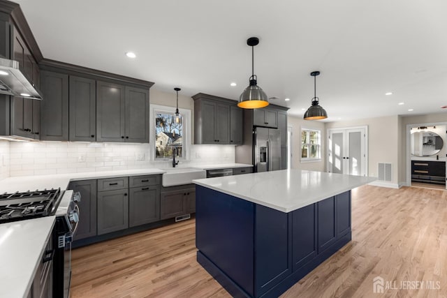 kitchen featuring sink, stainless steel appliances, decorative light fixtures, backsplash, and a kitchen island