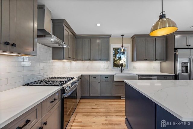 kitchen featuring wall chimney exhaust hood, light hardwood / wood-style flooring, pendant lighting, appliances with stainless steel finishes, and sink