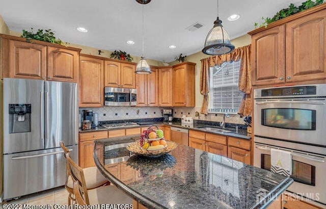 kitchen featuring stainless steel appliances, a kitchen island, a sink, visible vents, and tasteful backsplash