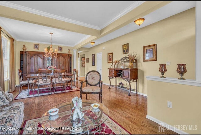 living room featuring wood finished floors, baseboards, ornamental molding, an inviting chandelier, and ornate columns