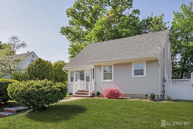 view of front facade with a shingled roof, fence, and a front yard