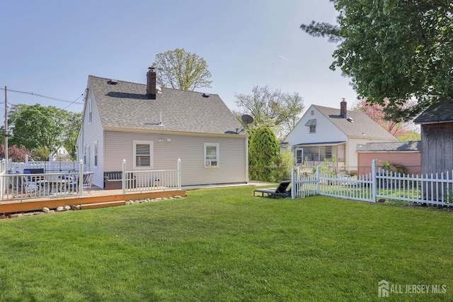 back of property with a lawn, a chimney, fence, a shingled roof, and a wooden deck