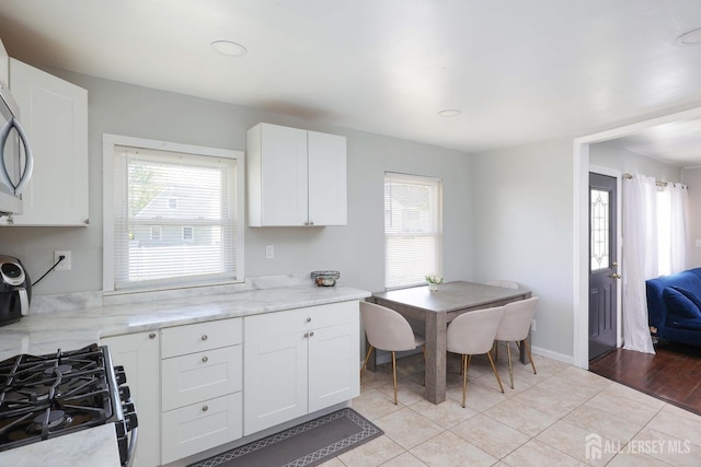 kitchen with range with gas stovetop, plenty of natural light, light stone counters, and white cabinets