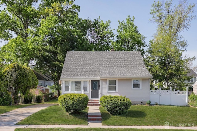 view of front of home with concrete driveway, a shingled roof, a front lawn, and fence