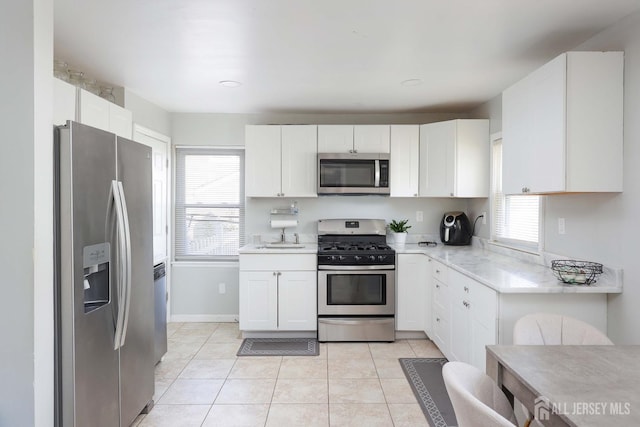 kitchen with baseboards, light stone counters, light tile patterned flooring, white cabinetry, and appliances with stainless steel finishes