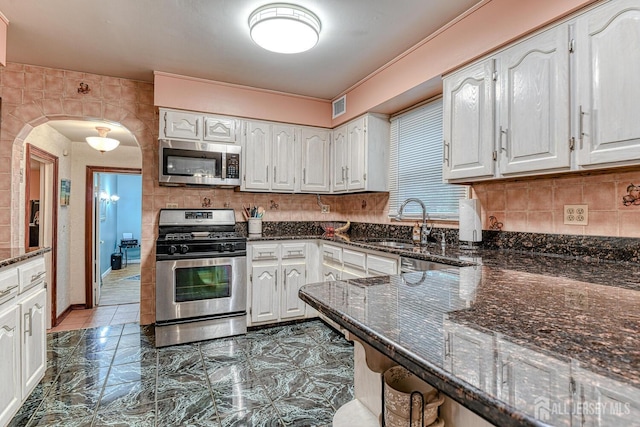 kitchen featuring stainless steel appliances, sink, dark stone countertops, and white cabinets