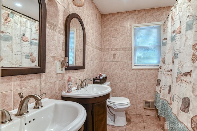 bathroom with toilet, tile patterned flooring, tile walls, and dual sinks