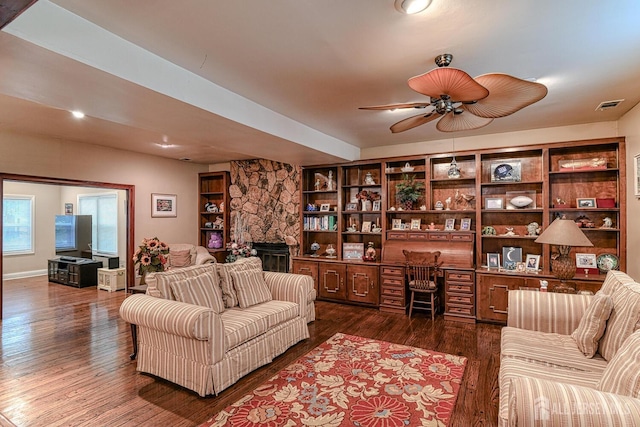 living room featuring ceiling fan, dark hardwood / wood-style flooring, built in desk, and a stone fireplace