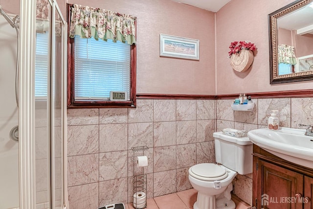 bathroom featuring a shower with shower door, tile walls, vanity, toilet, and tile patterned floors