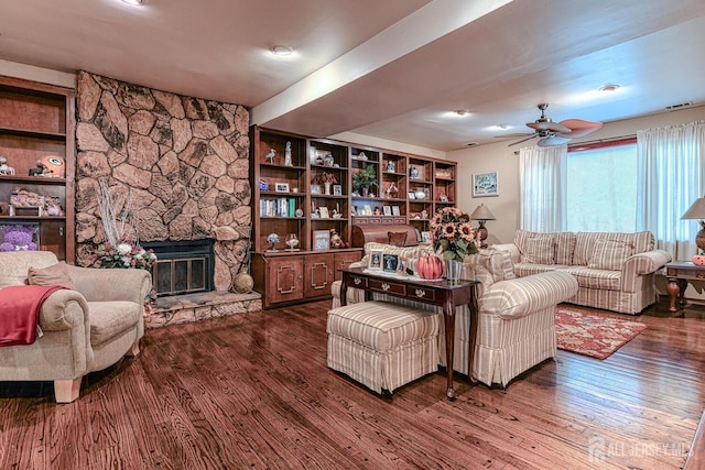 living room with a stone fireplace, dark hardwood / wood-style floors, and ceiling fan