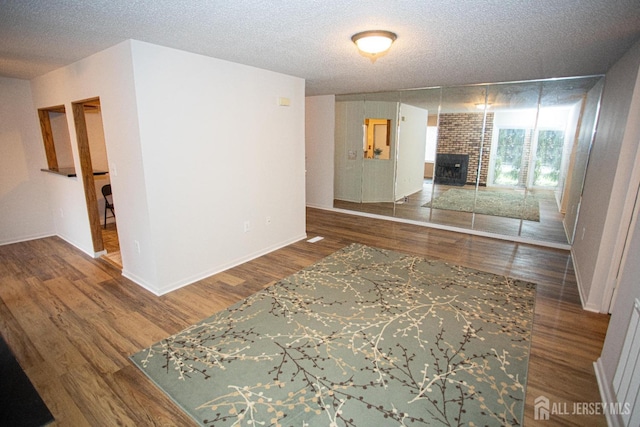 unfurnished living room featuring baseboards, wood finished floors, a textured ceiling, and a brick fireplace
