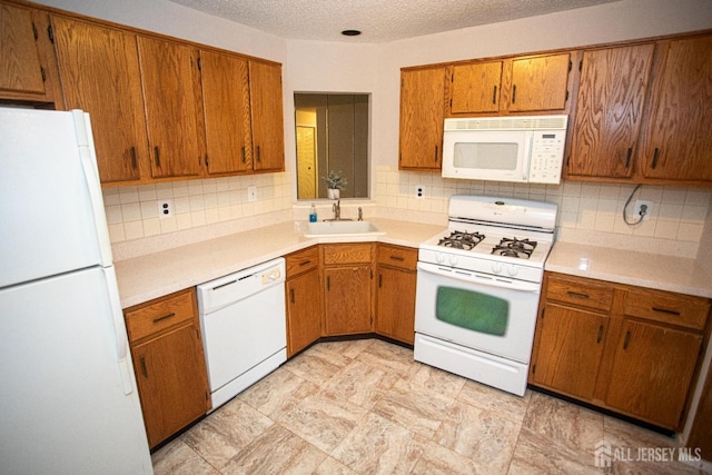 kitchen featuring decorative backsplash, brown cabinetry, white appliances, and a sink