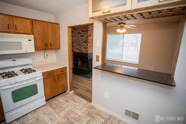 kitchen featuring brown cabinets, visible vents, white appliances, a brick fireplace, and ceiling fan
