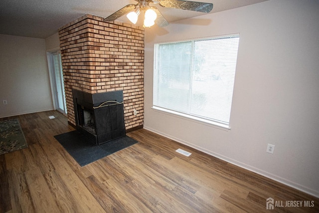 unfurnished living room featuring wood finished floors, visible vents, baseboards, a brick fireplace, and ceiling fan
