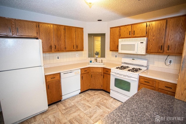 kitchen featuring backsplash, white appliances, a sink, and brown cabinets