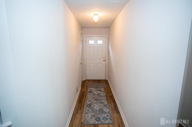 doorway featuring baseboards, wood finished floors, and a textured ceiling