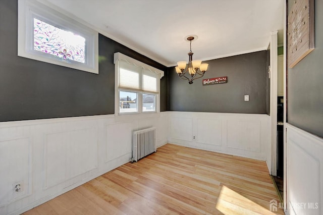 unfurnished dining area featuring a chandelier, light wood-type flooring, and radiator