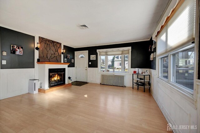 unfurnished living room with a stone fireplace, crown molding, radiator, and light hardwood / wood-style flooring